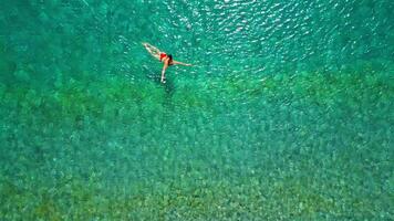 Woman in red swimsuit swims in the clear sea, top-down view. video