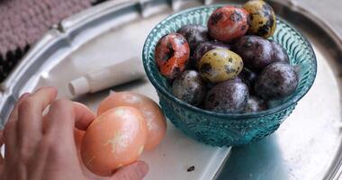 Decorative Easter eggs and quail eggs arranged in a colorful bowl with a hand holding additional pastel colored eggs photo
