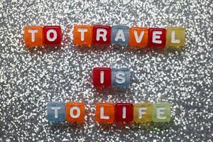 Travel as a vibrant expression of life captured in colorful letter blocks on a sparkling silver background photo
