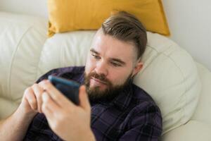 Bored lazy man relaxed and use smartphone for killing time alone in apartment - social media and gadget addiction concept photo