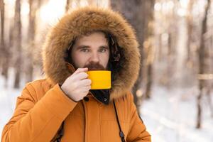 Man with yellow mug in snowy forest looking at camera. Mindfulness, warmth, and the human connection with nature during a quiet winter pause. Copy space photo