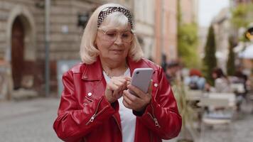 Senior woman use smartphone typing text messages browsing internet finishing work looking at camera video
