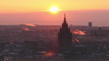 Sun rises over Riga, Latvia, illuminating the Latvian Academy of Sciences, rooftops with snow, and the Daugava River through morning mist and smoke trails. video