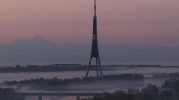 Serene morning in Riga, Latvia, with the Riga Radio and TV Tower, soft sunrise hues, and shifting mist creating a tranquil atmosphere. video