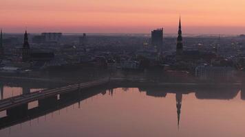 Serene morning in Riga, Latvia, with sunrise over the railway bridge, mist drifting on the Daugava River, and a cityscape of historic and modern buildings. video