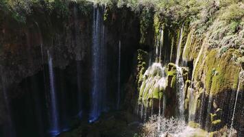 Vivid sunlight streaming over yerkopru waterfall, cascading through moss-covered rocky canyon with shadowy depths plunging into untouched wilderness landscape video