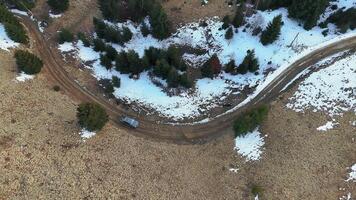 Top-down aerial of winding dirt road through snowy forest edge in Carpathian mountains, Off-road vehicle parked near turn in remote natural terrain with light snow patches video