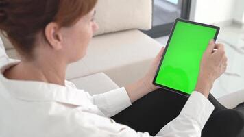 Redhead Woman Sitting on Sofa Holding Tablet with Green Chromakey Screen, Touching Display for App Mockup or UI Design, Modern Digital Technology and Wireless Communication in Bright Living Space. video