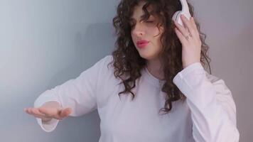 Happy and energetic female DJ with curly hair, wearing wireless headphones, mixing a new track and enjoying the process. High quality 4k footage video