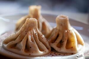 Traditional khinkali dumplings sprinkled with spices on a white plate and softly lit photo
