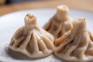 Three khinkali dumplings dusted with spices rest on a white plate highlighting their distinct pleated design photo