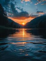 Sunset reflecting on a lake surrounded by mountains with concentric ripples in the water photo