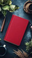 Red notebook, pen, coffee, plant, and other objects on a dark table photo