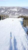 FPVdrone flight over snowy ski slope with skiers and mountain views on sunny day video