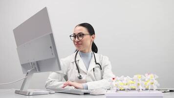 Portrait of female specialist, doctor works in a modern office using a computer. Models of the knee joint, pelvic floor and foot are on the table. Concept of orthopedic diagnostics. video