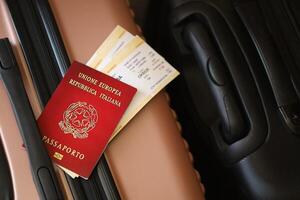 Italian passport with tickets lies on touristic suitcase close up in airport waiting hall photo