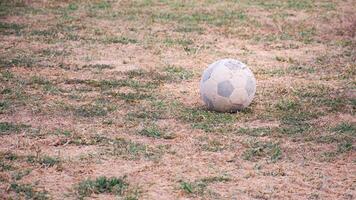 An old football with a peeling surface that reveals the threads, on an unsightly grass field in the countryside, background copy space. photo