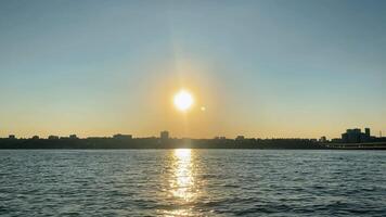 Sun setting over a cityscape reflected on water surface video