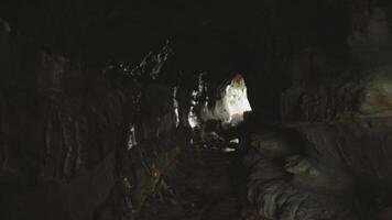 First-person view of narrow stone cave passage with visible light at the end. Mysterious underground tunnel with rough rocky walls and natural illumination. video