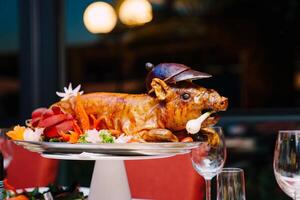 Roasted pig garnished with colorful vegetables lies on a platter on the table photo