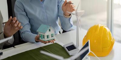 Sustainable Development and ESG Practices. A team discussing eco-friendly construction using a model house and wind turbines. photo