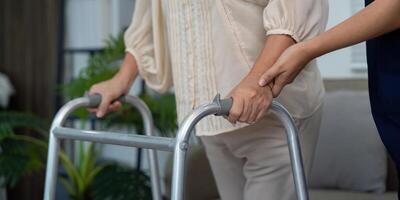 Supportive Care and Mobility Guidance. A caregiver holds the hand of an elderly patient while assisting her with a walker, enhancing safety and trust. photo