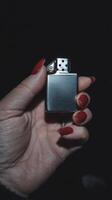 Hand holding a silver lighter with red nail polish in a dimly lit space during nighttime photo