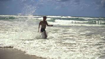 A joyful man runs along the shoreline through crashing waves, his carefree laughter carried by the sea breeze. Slow motion captures his exuberant dance with the ocean video