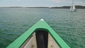 The bow of a ferry cuts through Sydney Harbour waters, with distant shoreline and sailing yachts visible. Demonstrates Australia's efficient public water transport system against iconic maritime video