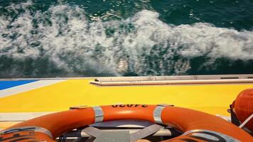 An overhead view captures a ferry or speedboat cutting through ocean waters, with the vessel's side, a lifebuoy, and churning waves visible below. Showcases maritime transport in action video