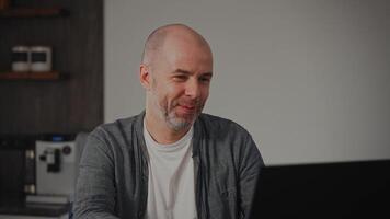 A middle-aged man looks at his laptop screen with a tender expression. He smiles softly while enjoying adorable content. The setting is cozy and homey. video