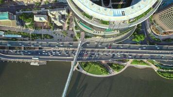 A drone camera points downward to capture a vibrant urban scene - a busy highway running alongside a winding river, flanked by towering skyscrapers and lively public spaces. video