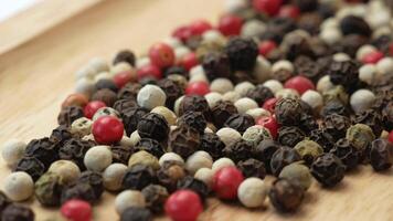 Spices a mixture of black, red, green and white pepper peas on a wooden background. Grains of dried multicolored pepper in close-up video