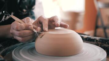 Potter, Craftsman is Working on Pottery Wheel,, Removes Extra Clay, Moulding a Clay Pot, Making a Vessel. Womens's Hands Close Up, dirty hands, pottery workshop, shelves, clay video