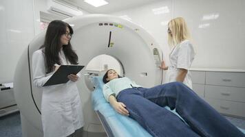 Female patient is undergoing CT or MRI scan under supervision of two qualified radiologists in modern medical clinic. Patient lying on a CT or MRI scan table, moving outside the machine 3 video