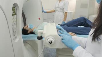 Patient is undergoing CT or MRI scan under supervision of two qualified radiologists in modern medical clinic. Patient lying on a CT or MRI scan table, moving outside the machine 5 video