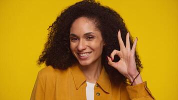 Smiling woman making OK hand gesture on yellow background video