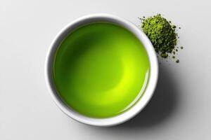 Vibrant green matcha tea in a white bowl with powdered matcha beside it on a plain surface photo