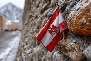 Flag of Austria displayed on a stone wall in a snow-covered village during winter photo