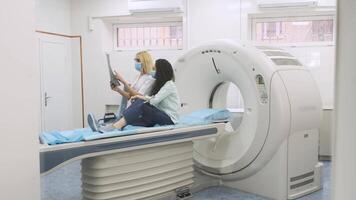 Woman doctor radiologist explains the results of CT scanning for young female patient, showing the snapshot with images, observing and analyzing CT scan in modern clinic beside modern CT scanner 13 video