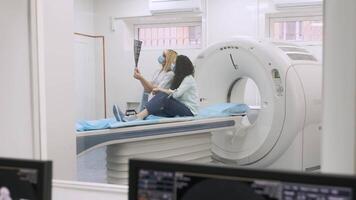 Woman doctor radiologist explains the results of CT scanning for young female patient, showing the snapshot with images, observing and analyzing CT scan in modern clinic beside modern CT scanner 14 video