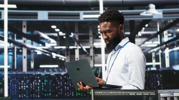Happy data center admin uses node tree programming on laptop to identify equipment performance issues. Cheerful server farm worker reviews data analysis graph to minimize hardware failures, camera B video