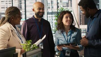 Relaxed multiethnic coworkers in office having fun chatting while reviewing documents, analyzing metrics. Smiling multiracial colleagues talking, working together, looking over paperwork, camera A video
