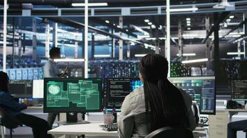 Server farm IT expert responds to security breach alert displayed on computer monitor, working to secure hardware. Data center employee attempts to protect equipment during cyberattack, camera A video