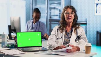 Senior medic consulting ill man in cabinet with isolated mockup screen, checking the hospital records to do another x ray scan interpretation. Old patient discuss with his physician. Camera B. video