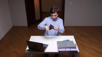 Office worker showing empty wallet at desk with laptop and folders video