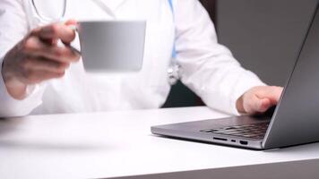 Doctor working on laptop and drinking coffee at desk video