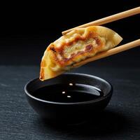A dumpling with chopsticks being held over a bowl of sauce photo