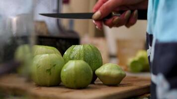 A hand grips a knife, slicing a dark green zucchini into diagonal pieces on a green cutting board. Several slices are already laid out, revealing white flesh. video