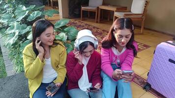 Three trendy women sitting and looking at their mobile phones during a holiday vacation. Checking messages, and social media while having fun. video
